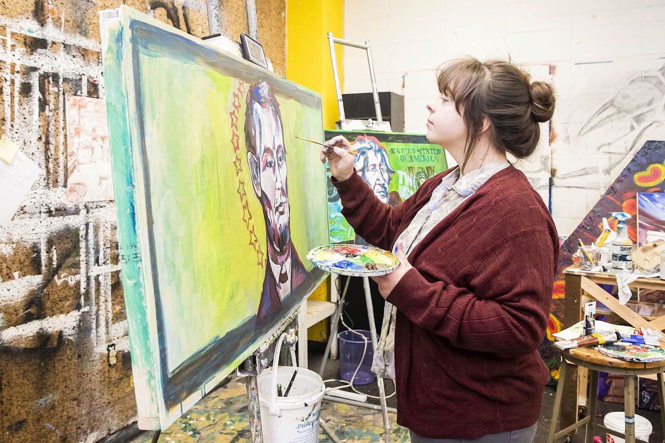 EKU student standing, adding to a large painting. 