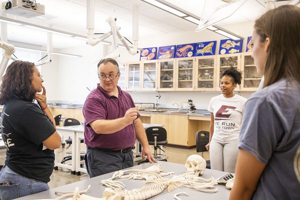 A professor and three students discuss a model of a human skeleton