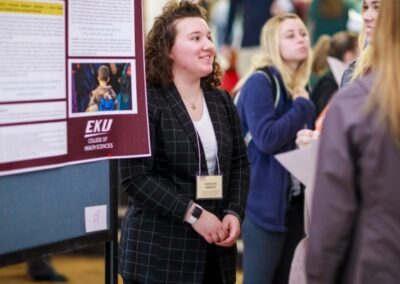 a student stands beside her research poster at Scholars Day 2022