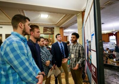 a student discusses his research poster with other students at Scholars Day 2022