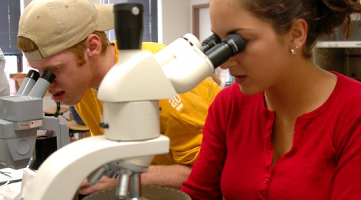 Two students look through microscopes.