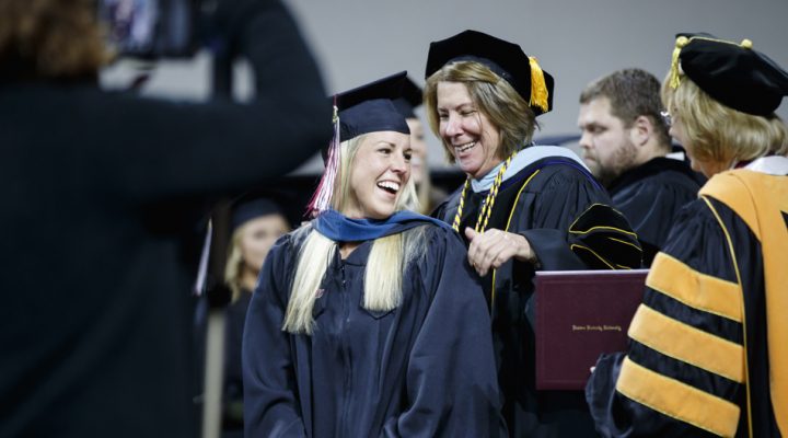 Student at graduation having stole place on neck by professor.