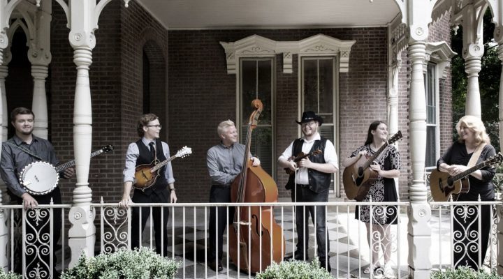 musicians with a banjo, mandolin, bass, and guitars performing on a front porch
