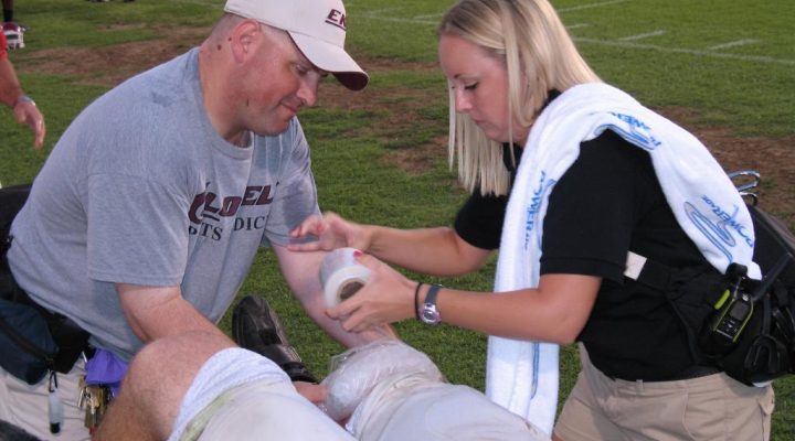 An image of a Eastern Kentucky University football player getting a knee wrapped on the field.