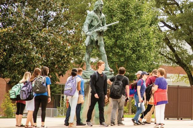 A large group of students walking and standing around the Daniel Boone statue on EKU's campus