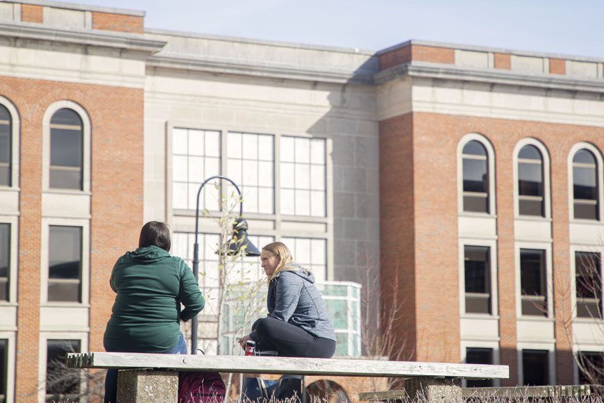 Students hang out on a bench outside of the Library facing Noel Reading Porch
