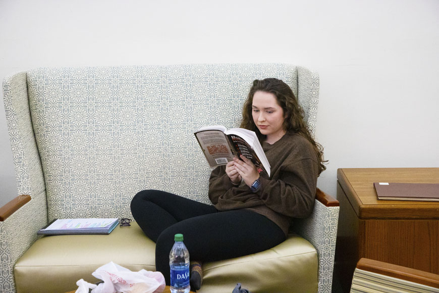 A student reads a book on a couch in the library. 