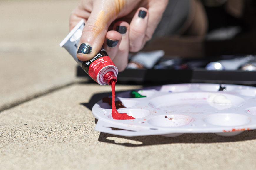 Close up of Ashley pressing red paint of tube to her pallet