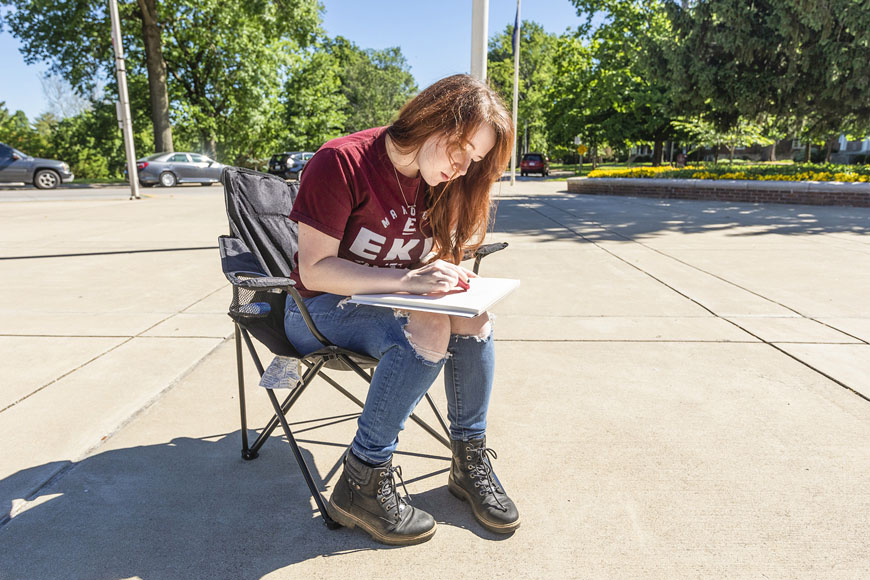 2020 graduate Ashley Fletcher sitting on a chair erasing sketchbook outside
