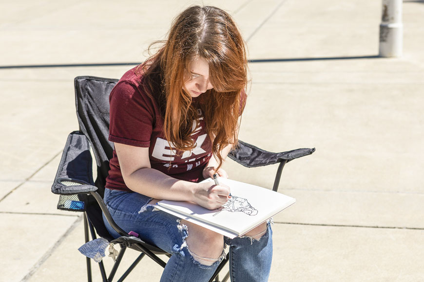 Ashley Fletcher sitting in chair on Keen Johnson plaza adding pen to sketchbbook