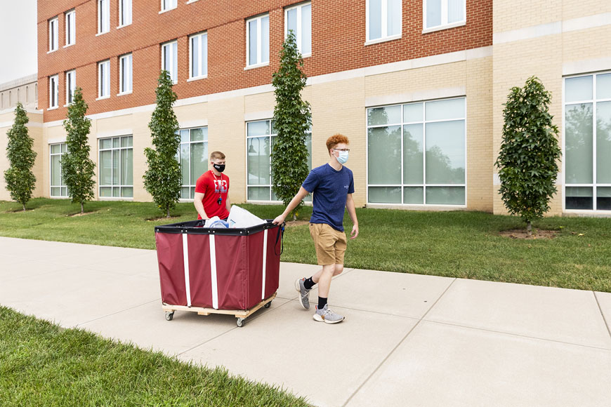 Two students rolling in cart of belongings into Martin Hall during Move in week