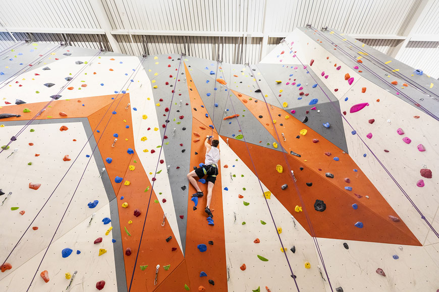 Student climbing in the middle of the vibrant rock wall inside the Rec Center