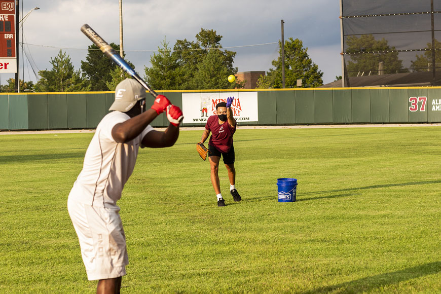 Two students pitching and hitting baseball on the Combs Baseball field