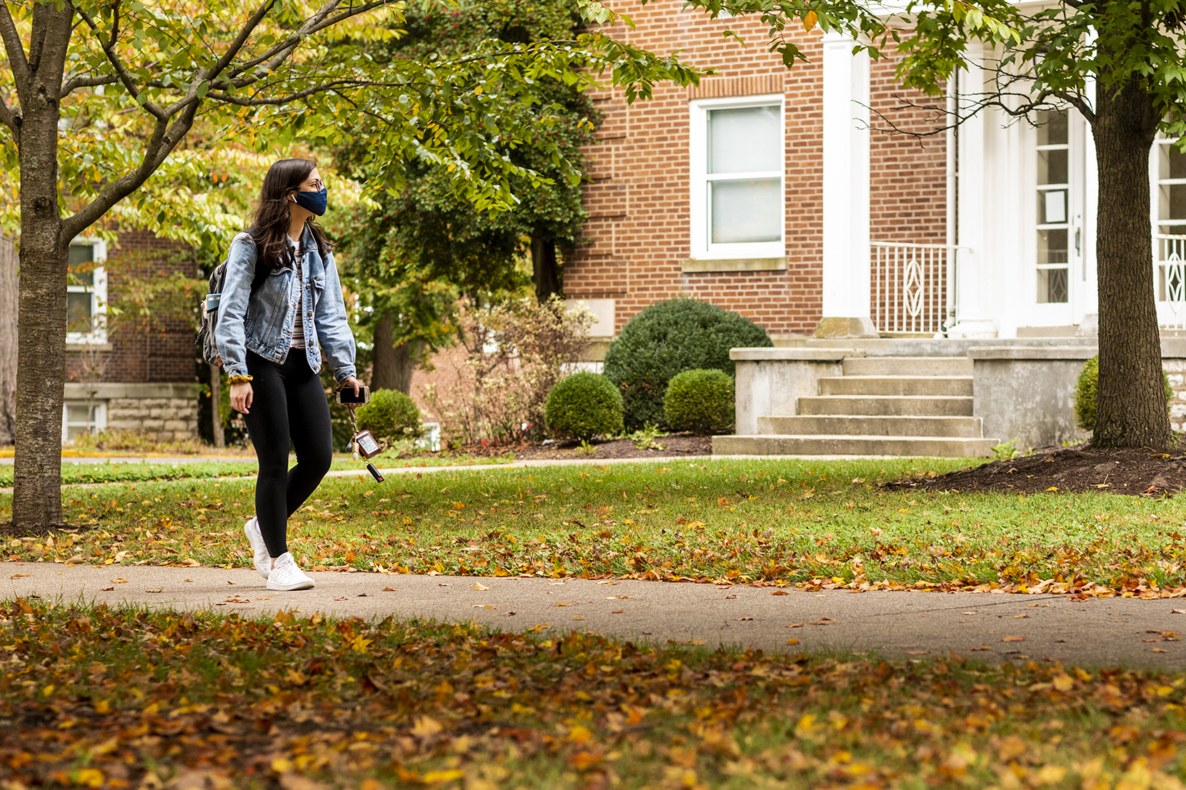 Student walking in front of Palmer building through trees with leaves on ground