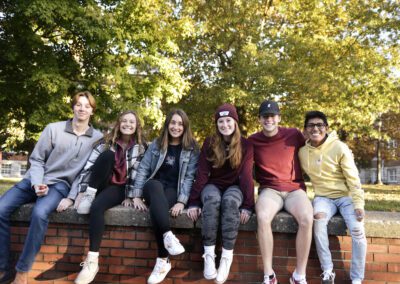 Group of students sit on stone fence smiling