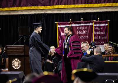 Student in cap and gown mid-handshake with EKU President McFaddin