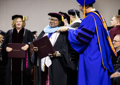 A student holding diploma surrounded by faculty in applause