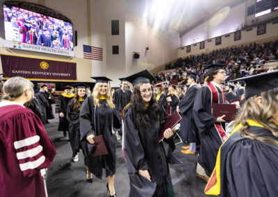 Students in black robes holding diplomas walk down aisle