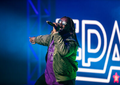 T-Pain performs wearing aviator sunglasses, a purple shirt, and green jacket
