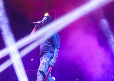 Waka Flocka Flame performs holding a microphone on a stage lit with purple and pink lights