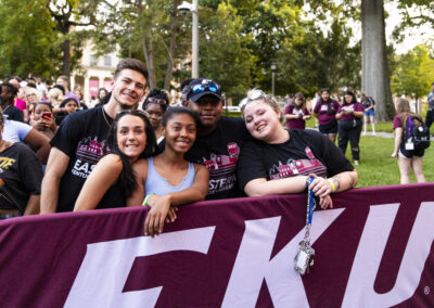 A group of students wearing EKU shirts pose together before an maroon 'EKU' banner