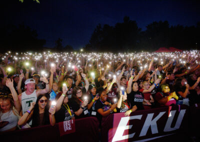 A crowd of students holding up cellphones with the flashlight on behind an 'EKU' branded barrier