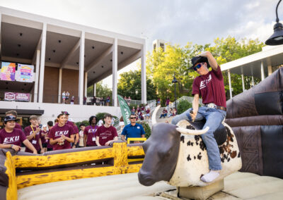 Students look on as a staff member rides a mechanical bull