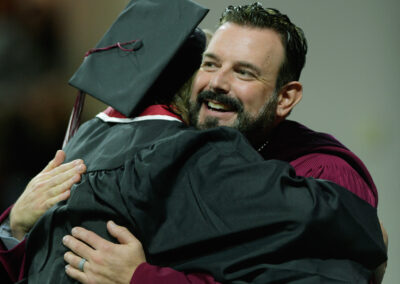 A graduate at Eastern Kentucky University's Fall 2023 Commencement ceremony hugging the president.