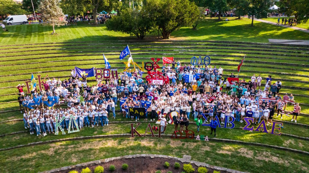 sorority and fraternity students pose outside with their flags and letters