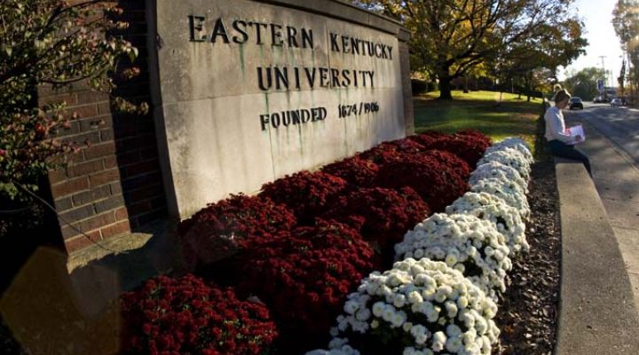 The Eastern Kentucky University sign, with a student reading in front of it.