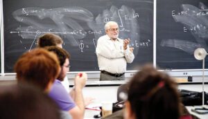 Bearded professor in tan dress shirt conducting a lecture in front of his class