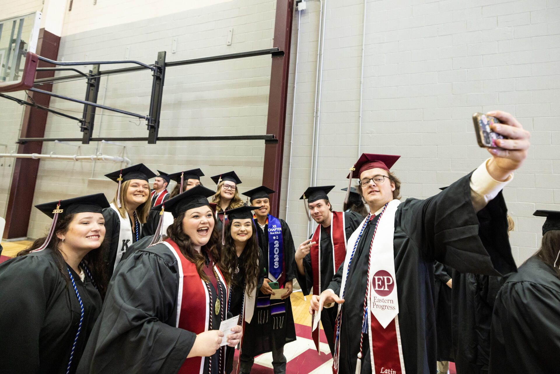 Smiling graduates with diplomas walking down aisle during commencement ceremony
