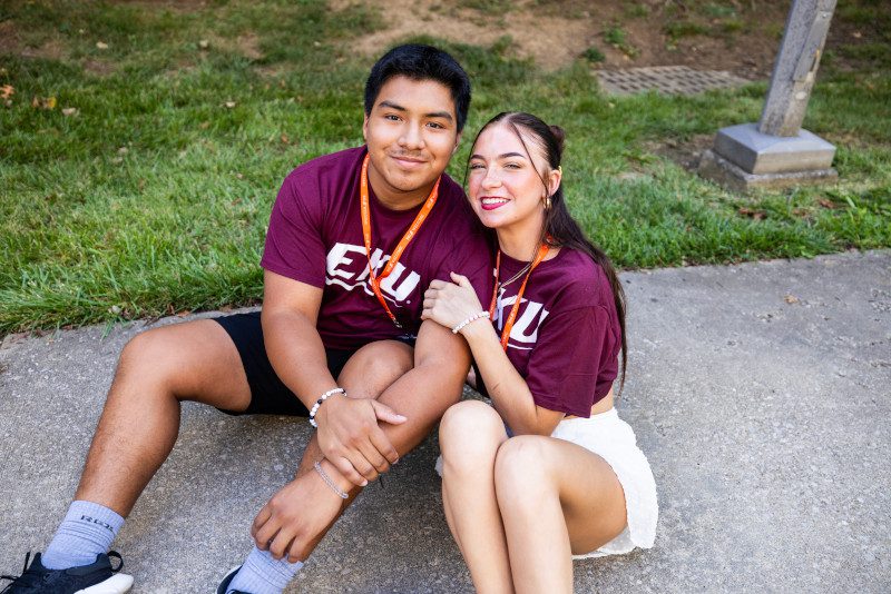 Two EKU students (a man and a woman) are posing for a photo while sitting on the ground together