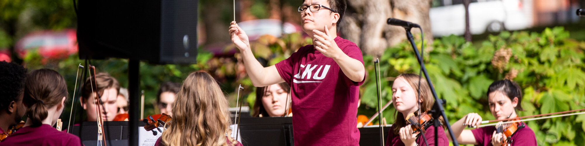 a student conducts an EKU ensemble playing violins outside