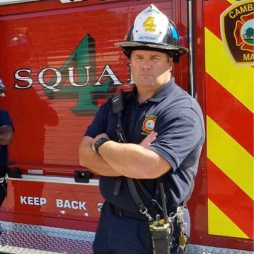 Bryan B. O'Neil wears his fire helmet and stands next to a fire engine.