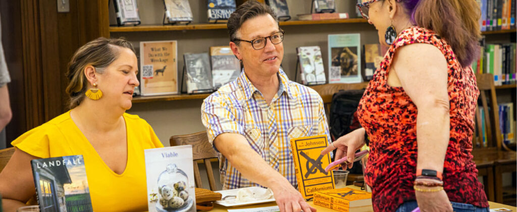 Header image of two authors sitting at table with their books