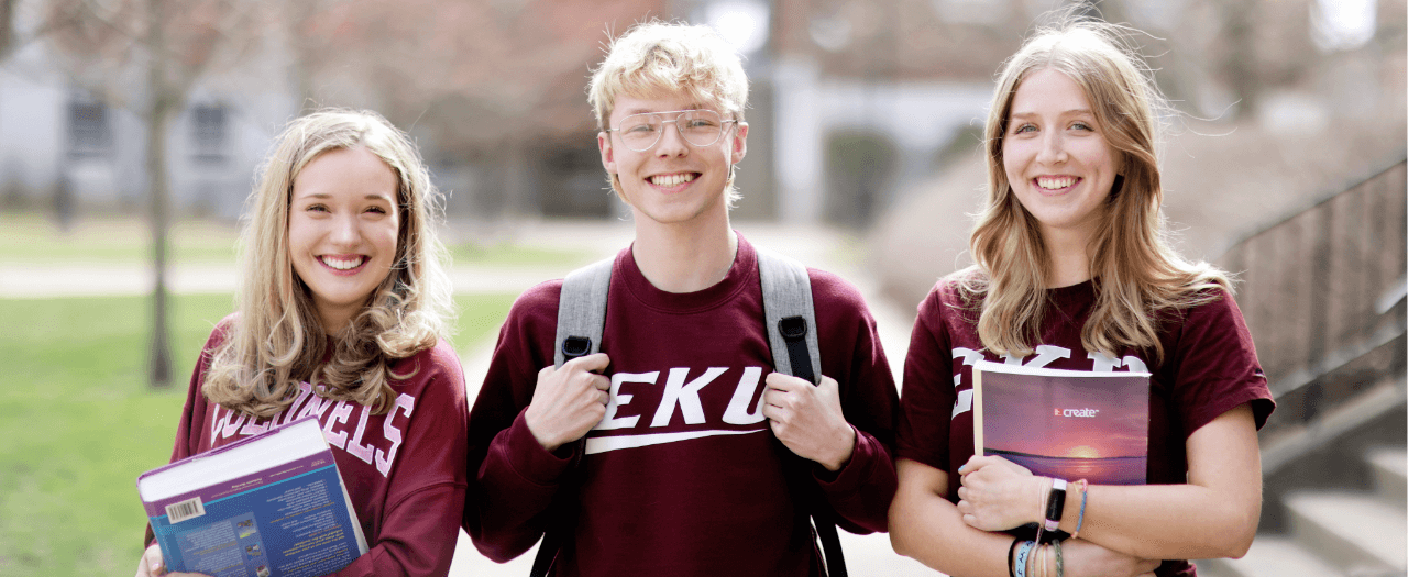 three smiling EKU students with books and backpacks wearing EKU shirts
