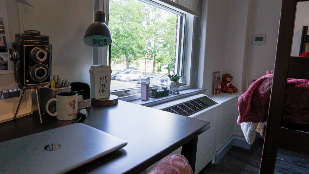 a student desk with various study materials and the view of trees out of the room's window