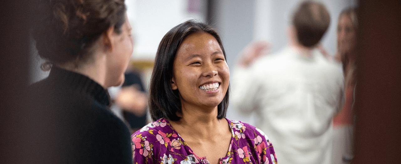 smiling woman in the center of the frame side view of a person on the left side of the frame with people blurred out in the background