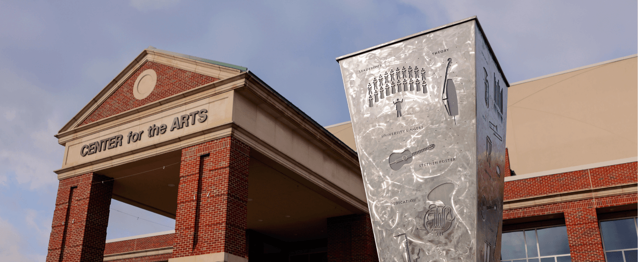 metal sculpture with engraved images of musical isntruments and a choir in foreground with the entrance to the EKU Center for the Arts in the background