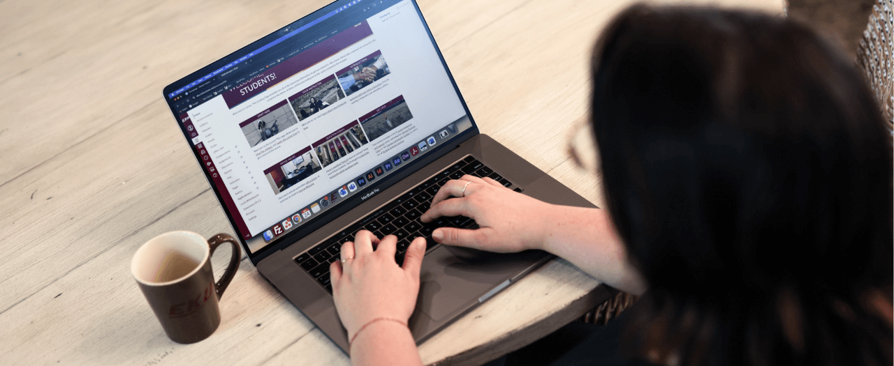 photo taken looking over a person's shoulder as they type on a laptop with a cup of coffee next to it
