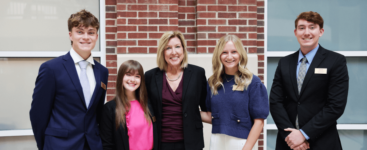 five people stand in front of the college of business. Jeri Isbell in the center, flanked by 4 students
