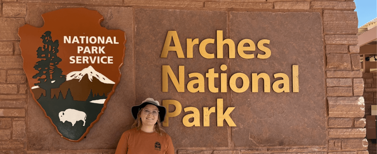 person stands in front of arches national park sign