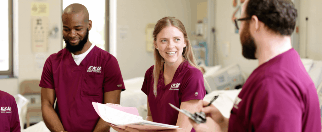 three people in eku maroon nursing scrubs happily chat in a clinical setting