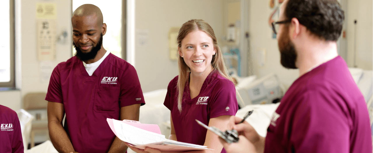 three people in eku maroon nursing scrubs happily chat in a clinical setting