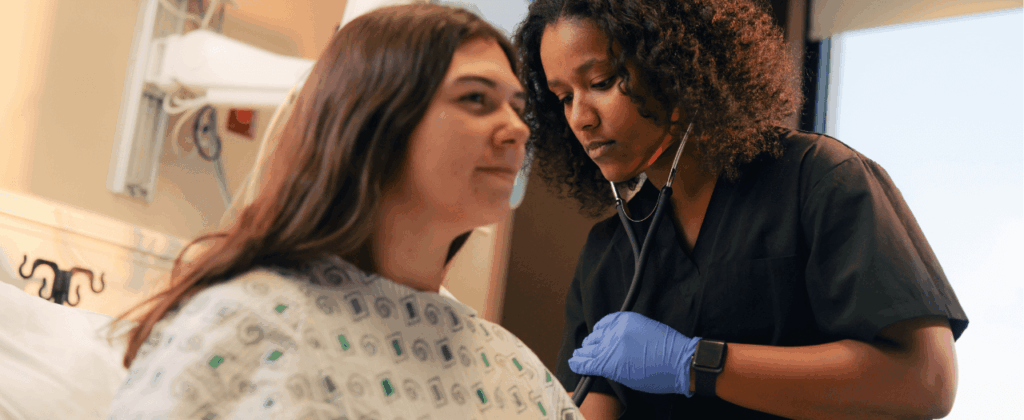 medical professional uses stethoscope to examine patient in hospital gown