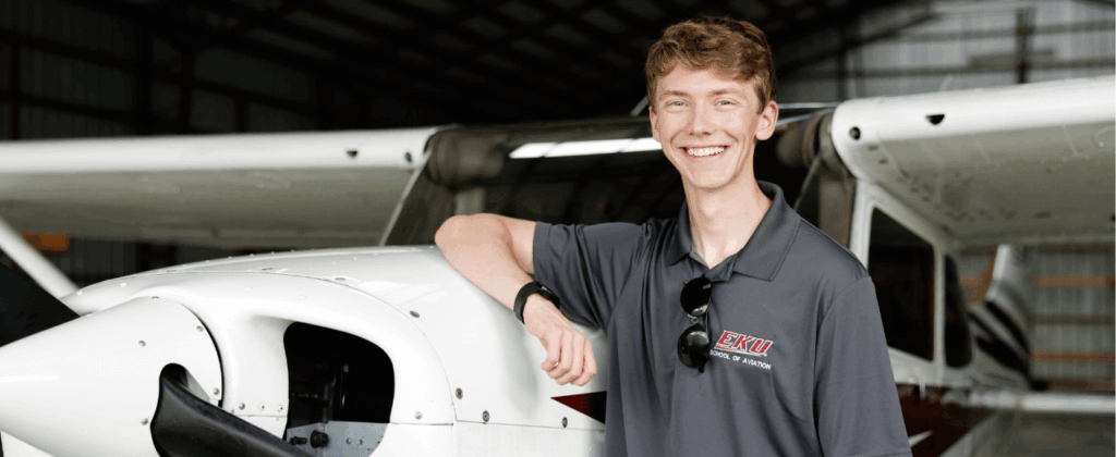 student in EKU shirt stands next to a propeller on a plane