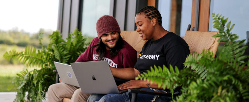 A male and a female student sit outside and work together on a laptop.