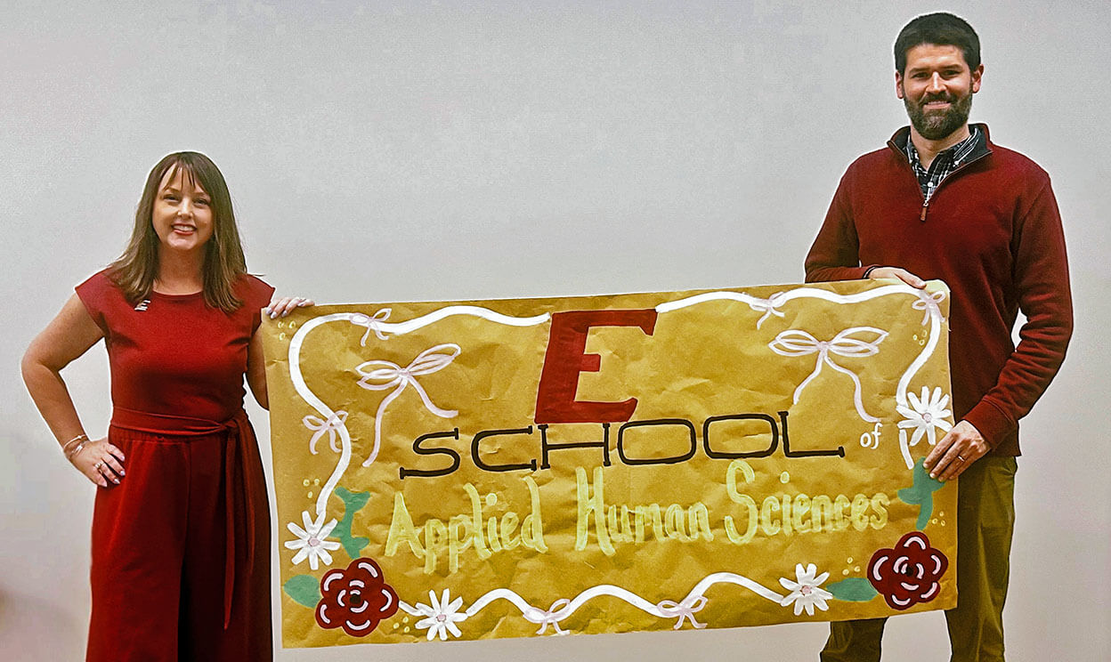 Header image of two faculty members holding banner for School of Applied Human Services