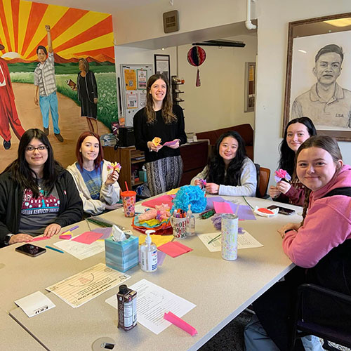 Six female students gather at a table to make a craft project